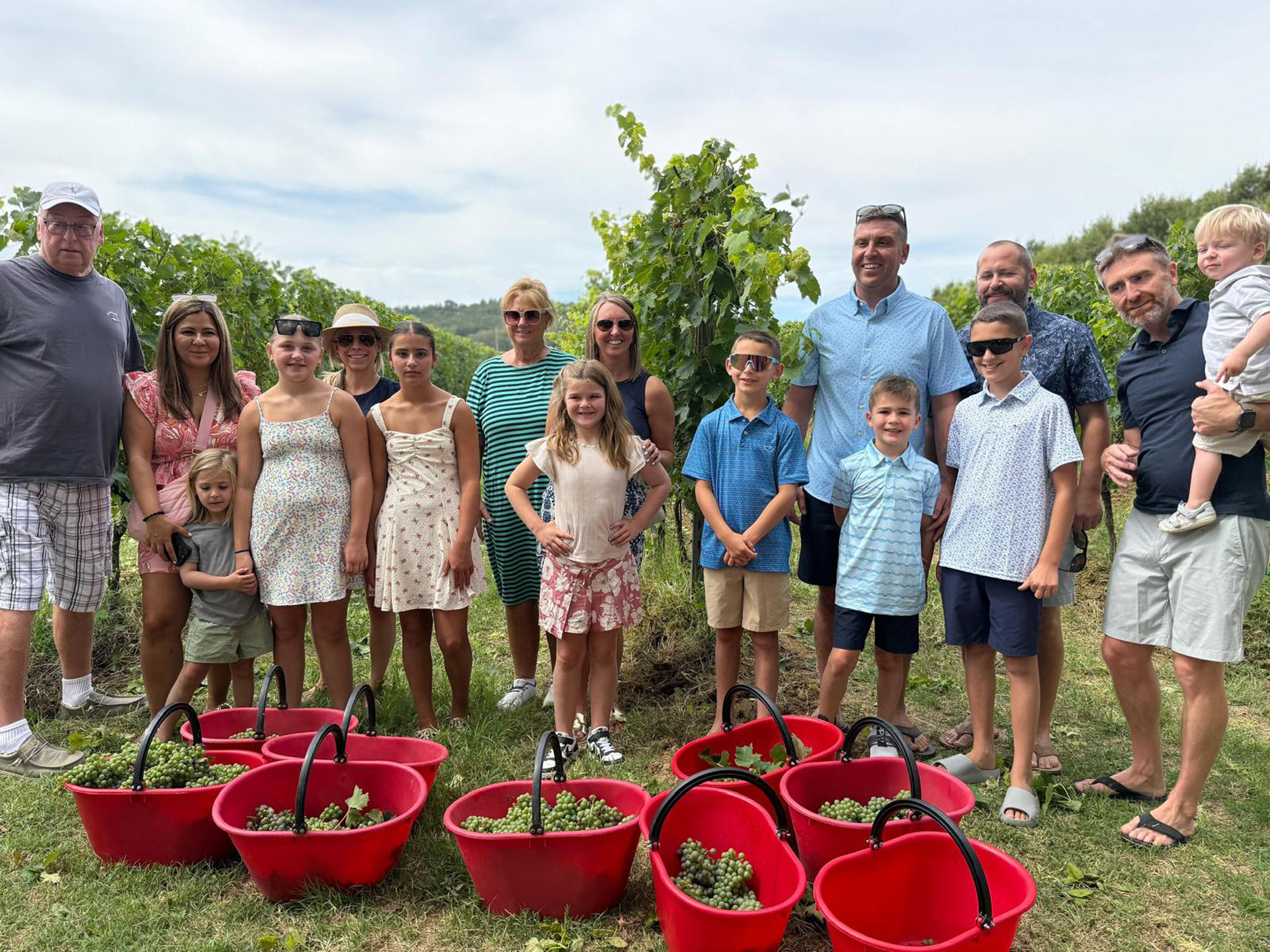 Una famiglia in vigna dietro una fila di cesti rossi della vendemmia a Tenuta Torciano